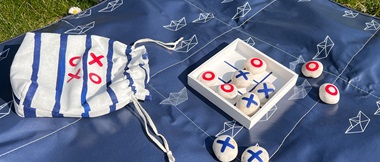 Mini wooden and pebble tic-tac-toe game on blue picnic mat