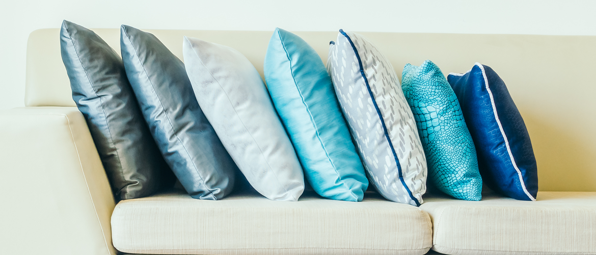 Blue-toned cushion covers with piping, arranged on a sofa.