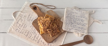 Cake on a cutting board surrounded by printed kitchen textiles