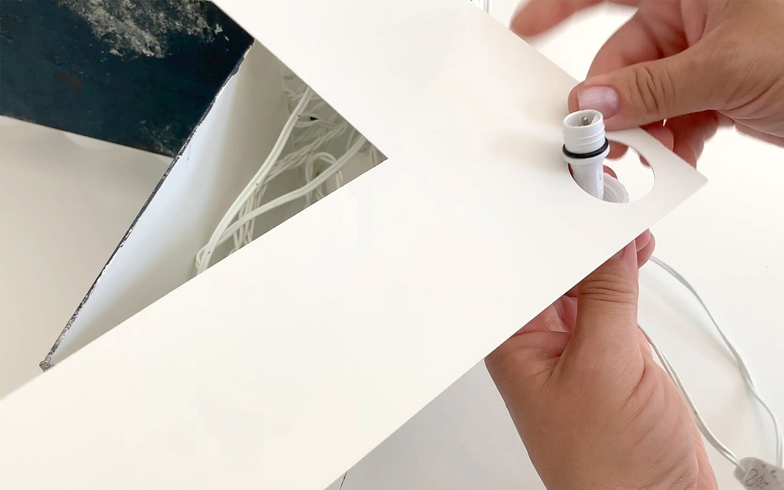 hand threading wire of string lights through small hole