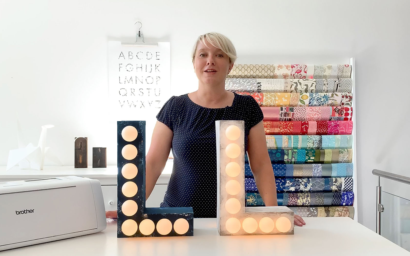 Blonde short haired woman in craft studio behind two L shaped lights
