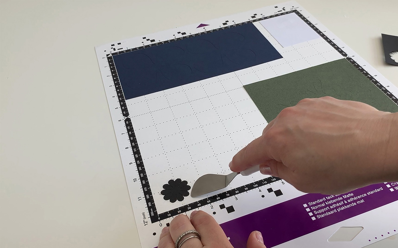 A hand with small spatula removing coloured paper from a ScanNCut mat