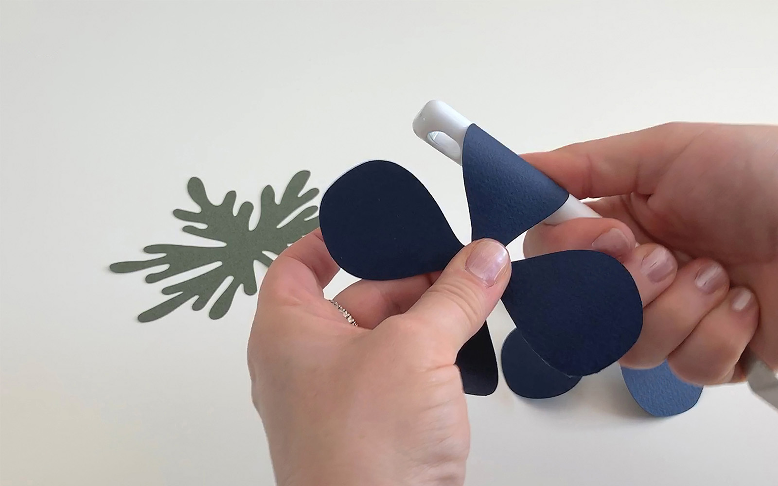 A hand holding a blue paper flower curling the petals round a pen