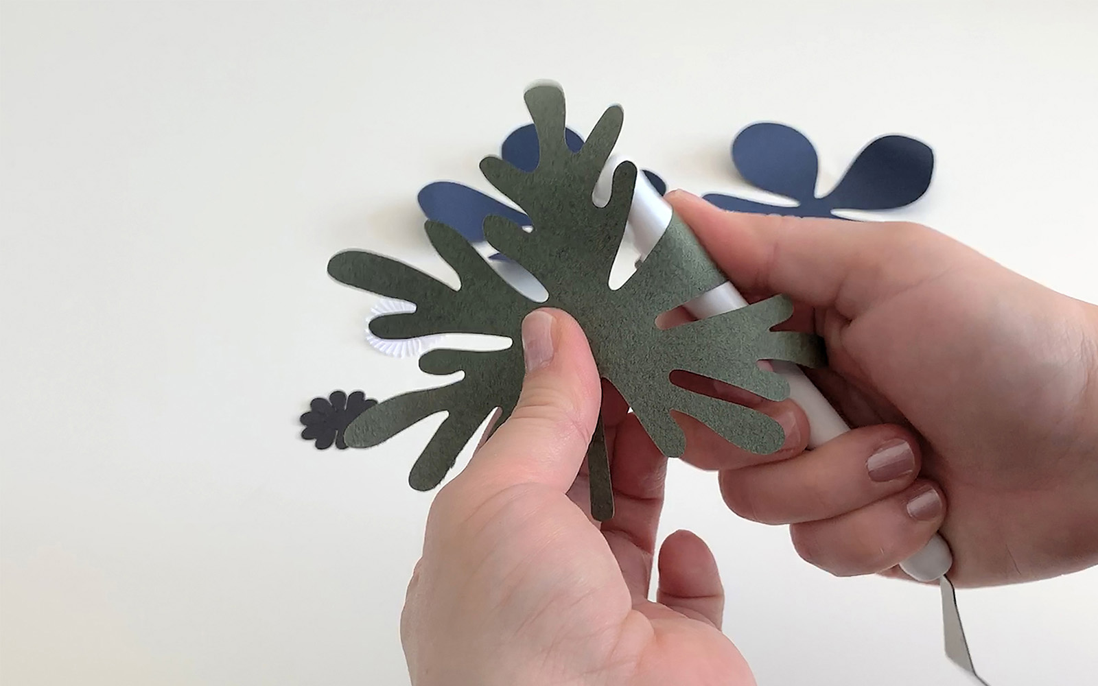 A hand holding a green paper leaf curling the round a pen