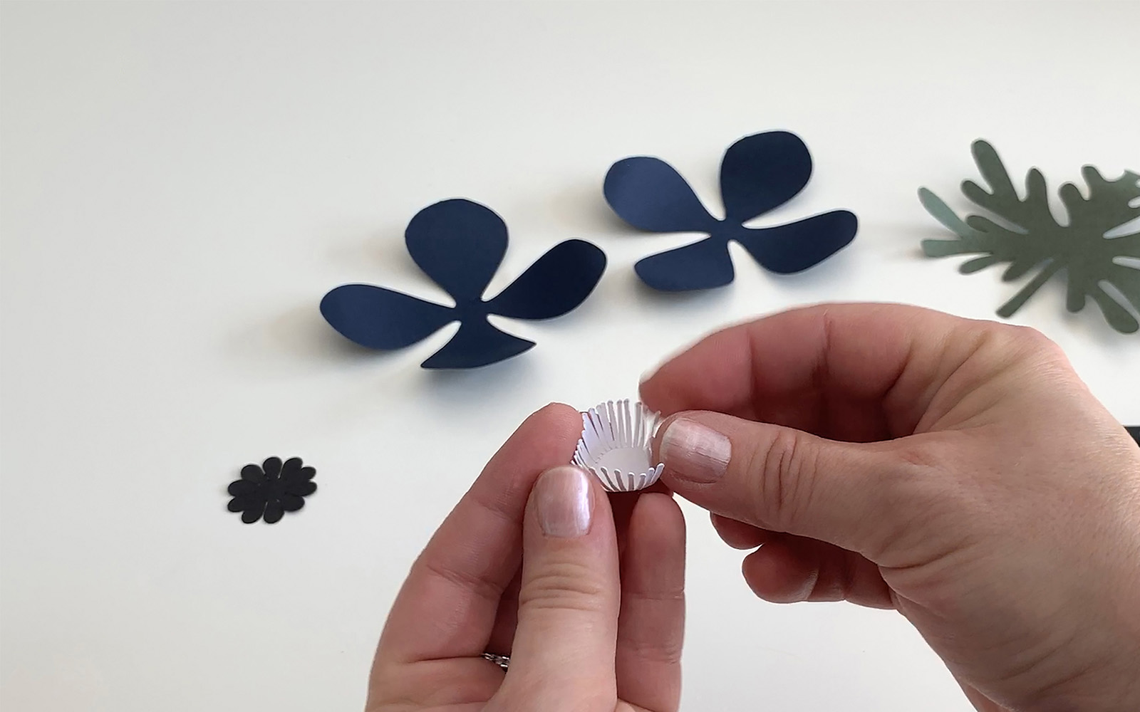 A hand holding a white papercut stamen and bending with fingers