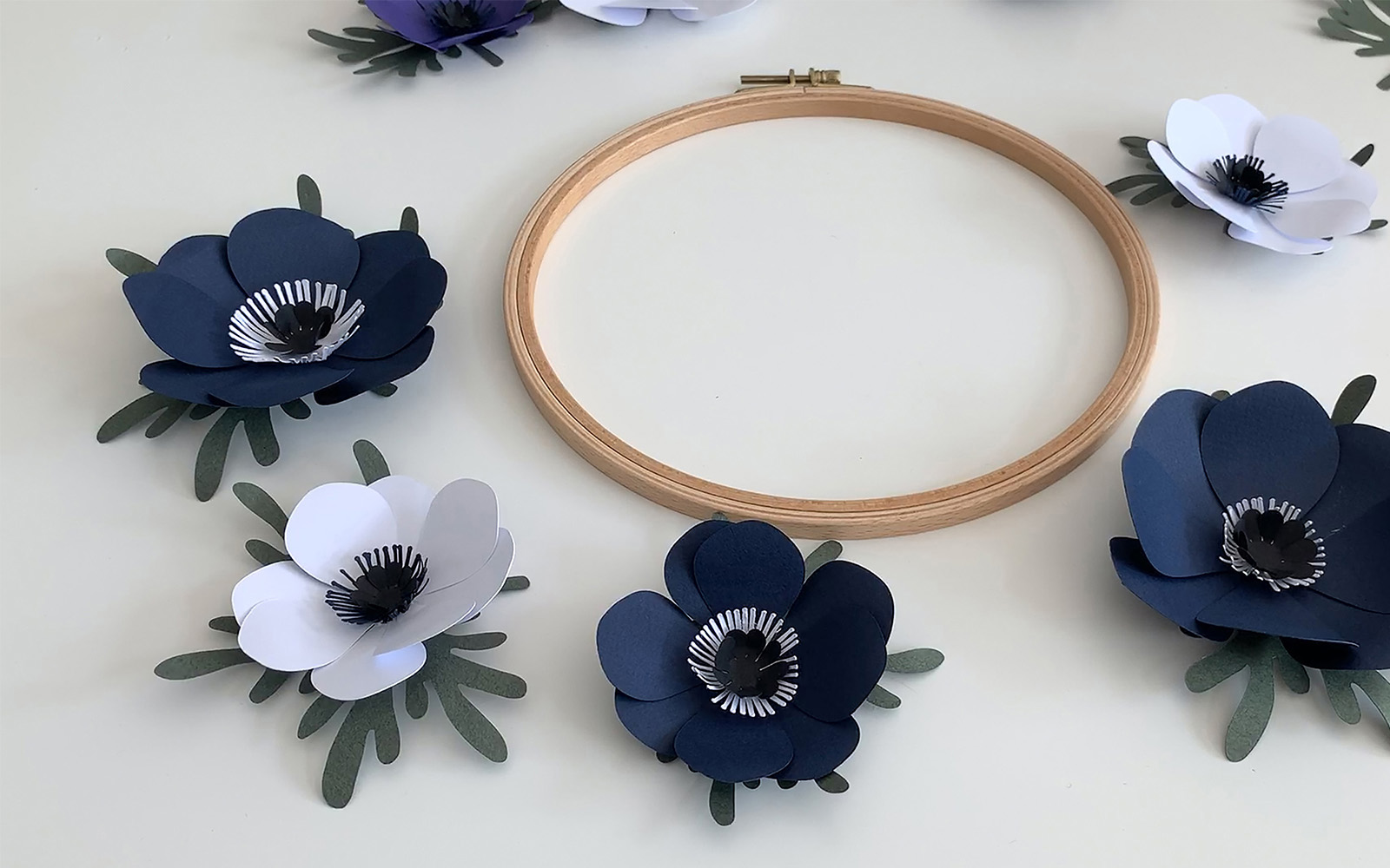 A wooden embroidery hoop with blue and white paper flowers around