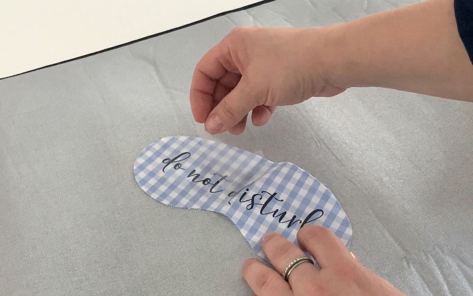 Hand peeling clear film from black text on blue sleep mask
