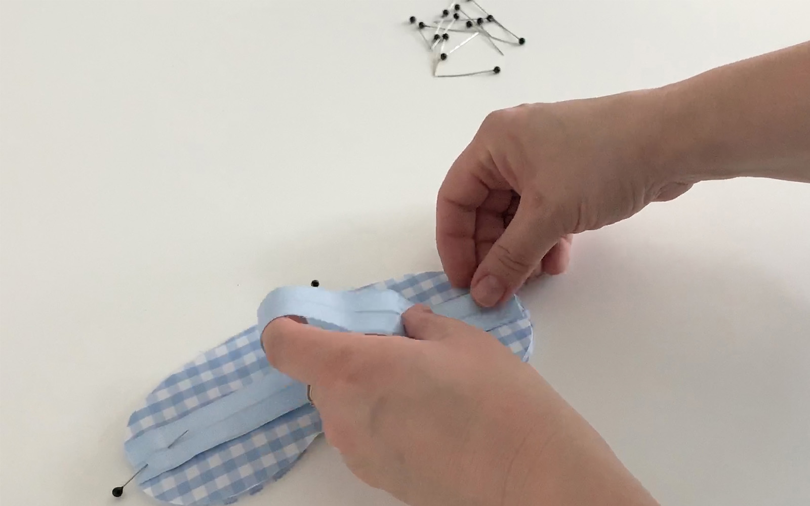 hands pinning blue elastic to the back of a blue cotton sleep mask