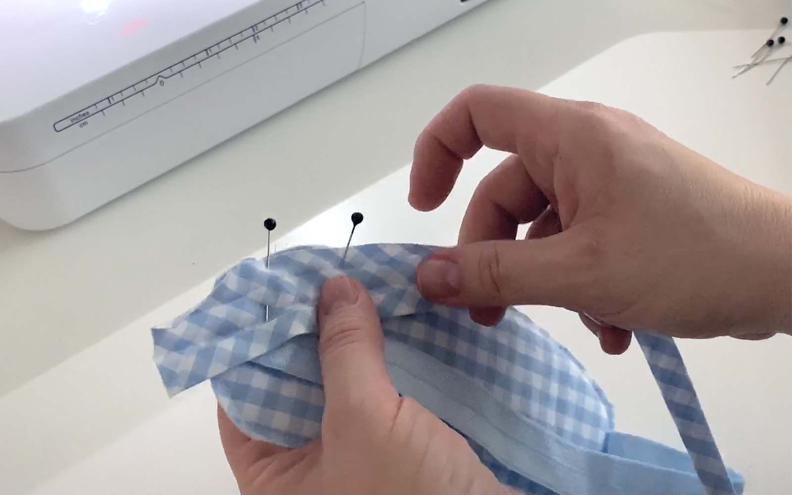 hands pinning blue check bias tape to edge of blue sleeping mask