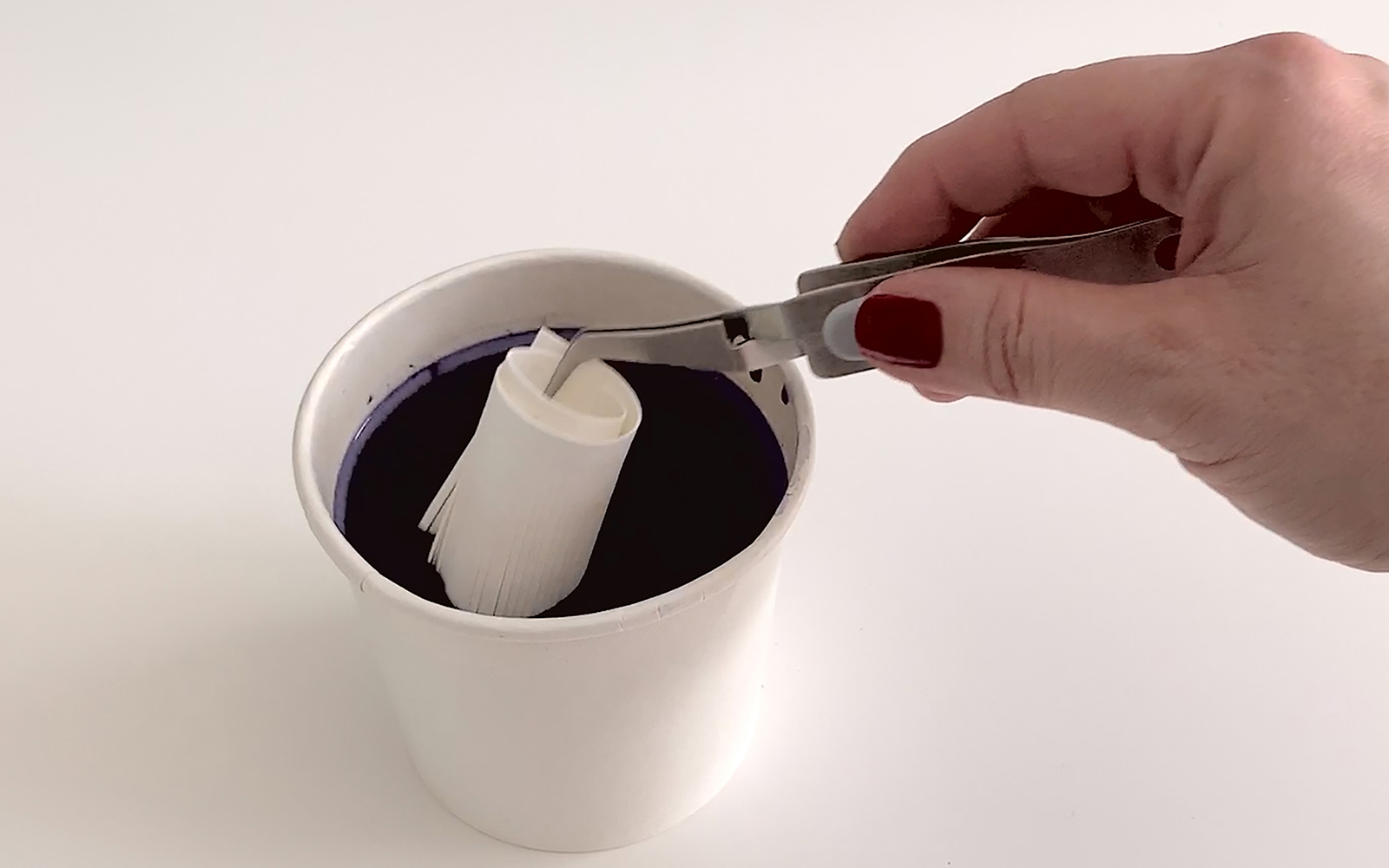 hand dipping tasselled vegan leather into cup of dark textile dye
