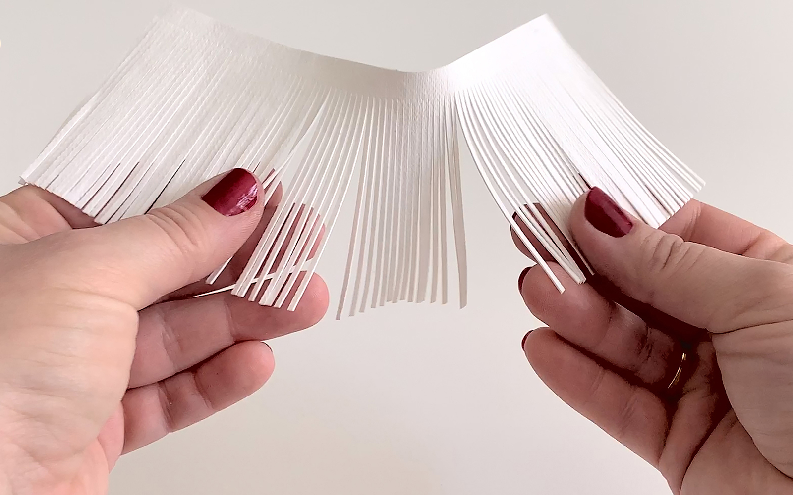 hands hold up a tasselled rectangle of white vegan leather