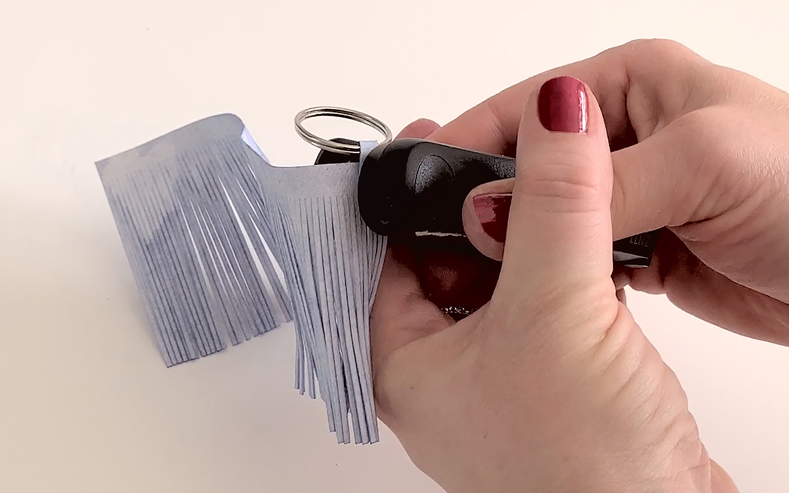 Blue metallic tassel being stapled to silver metal keyring
