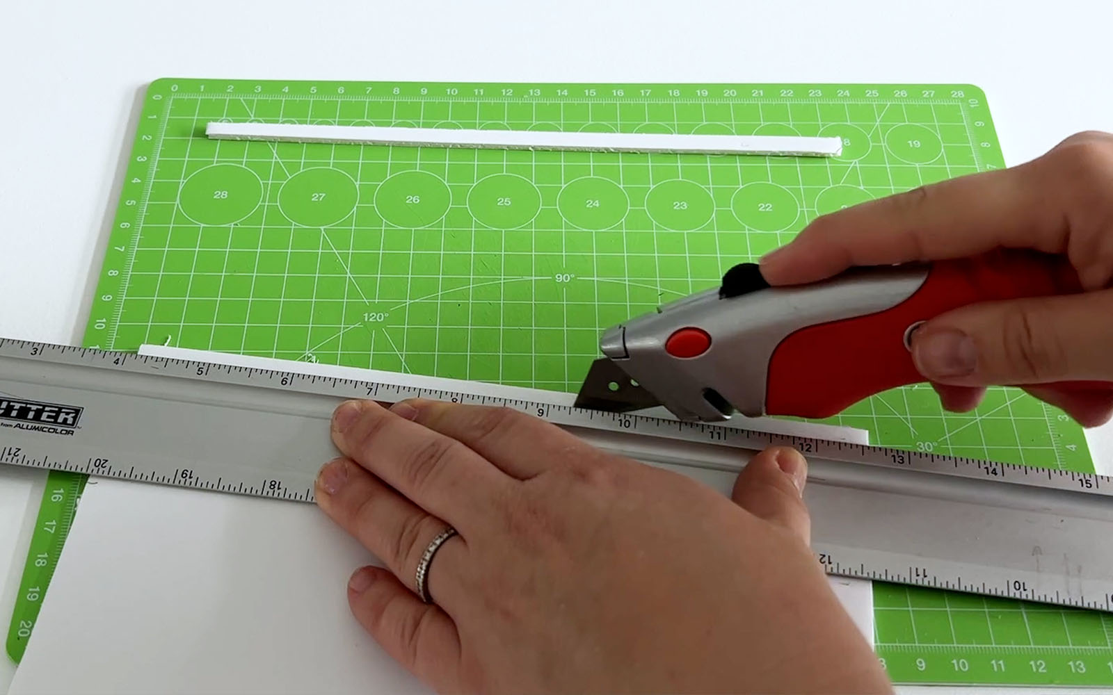 Foam board being cut into strips with a craft knife on a green cutting mat