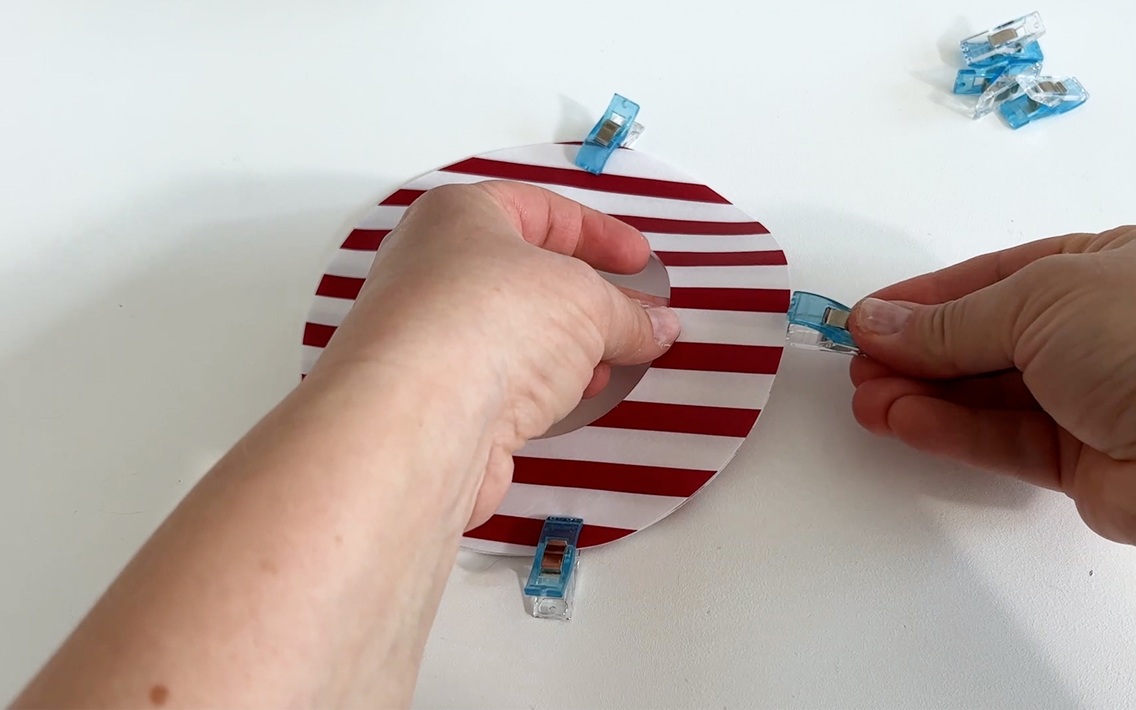 Assemblage de deux O en toile cirée rayée rouge et blanche à l'aide de pinces à tissu. 