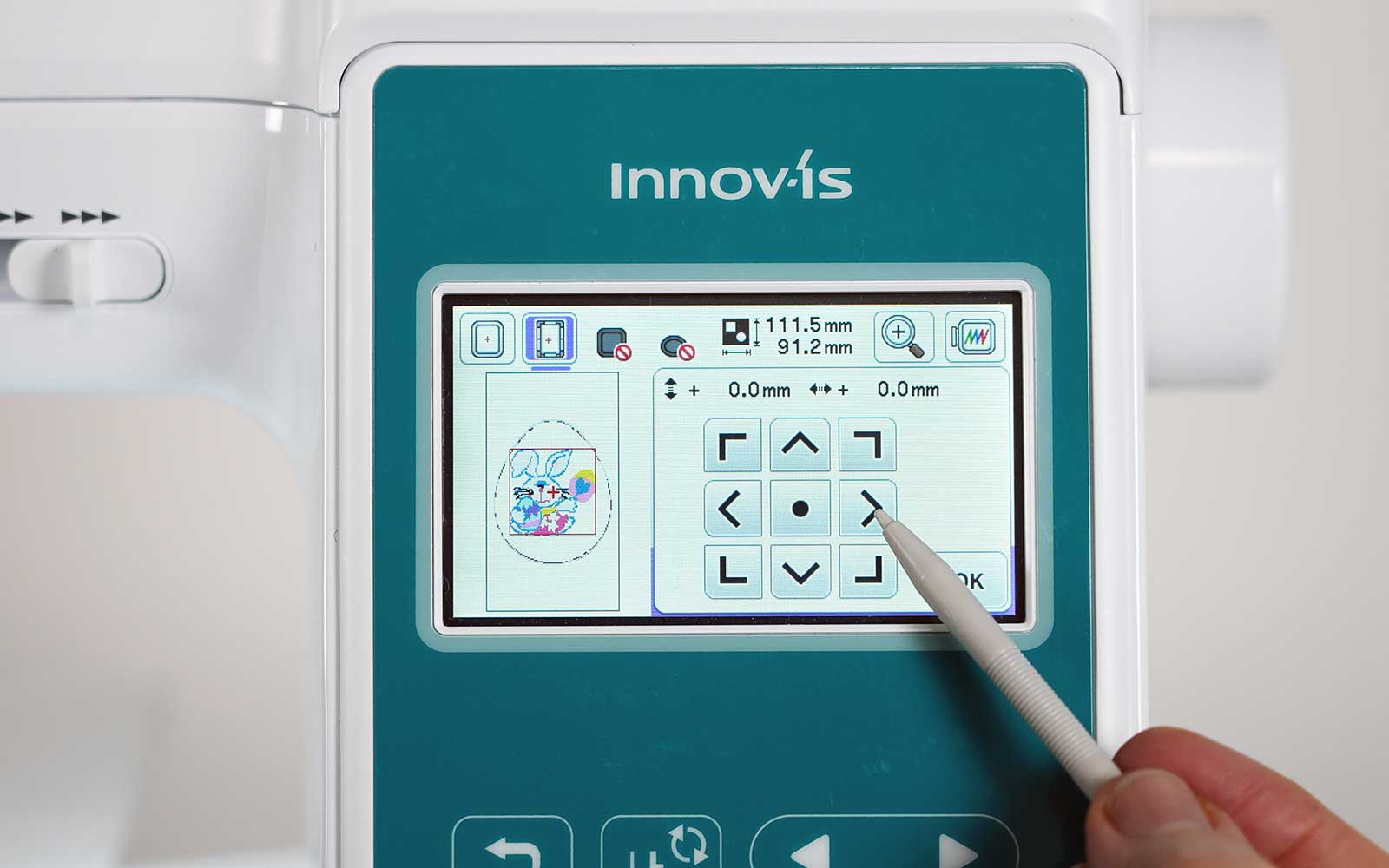 Stylus pointing at Brother embroidery machine screen with arrows