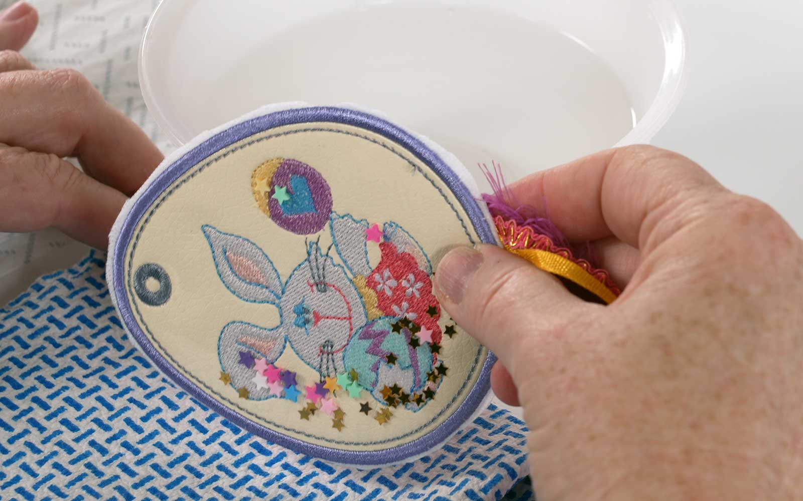  Hands dabbing embroidered pale yellow Easter egg onto wet dishcloth