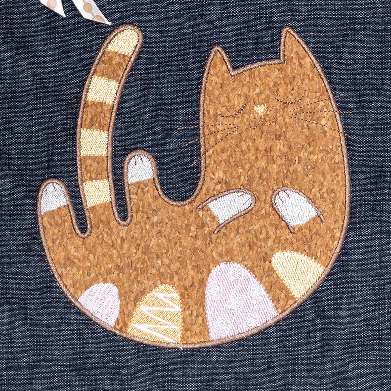 cork appliqué cartoon cat lying on back with smile on dark blue denim