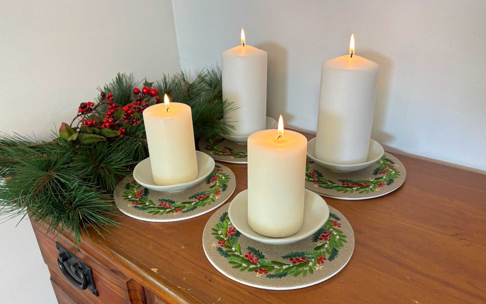 Quatre bougies sur des dessous brodés avec une broderie de couronne de Noël