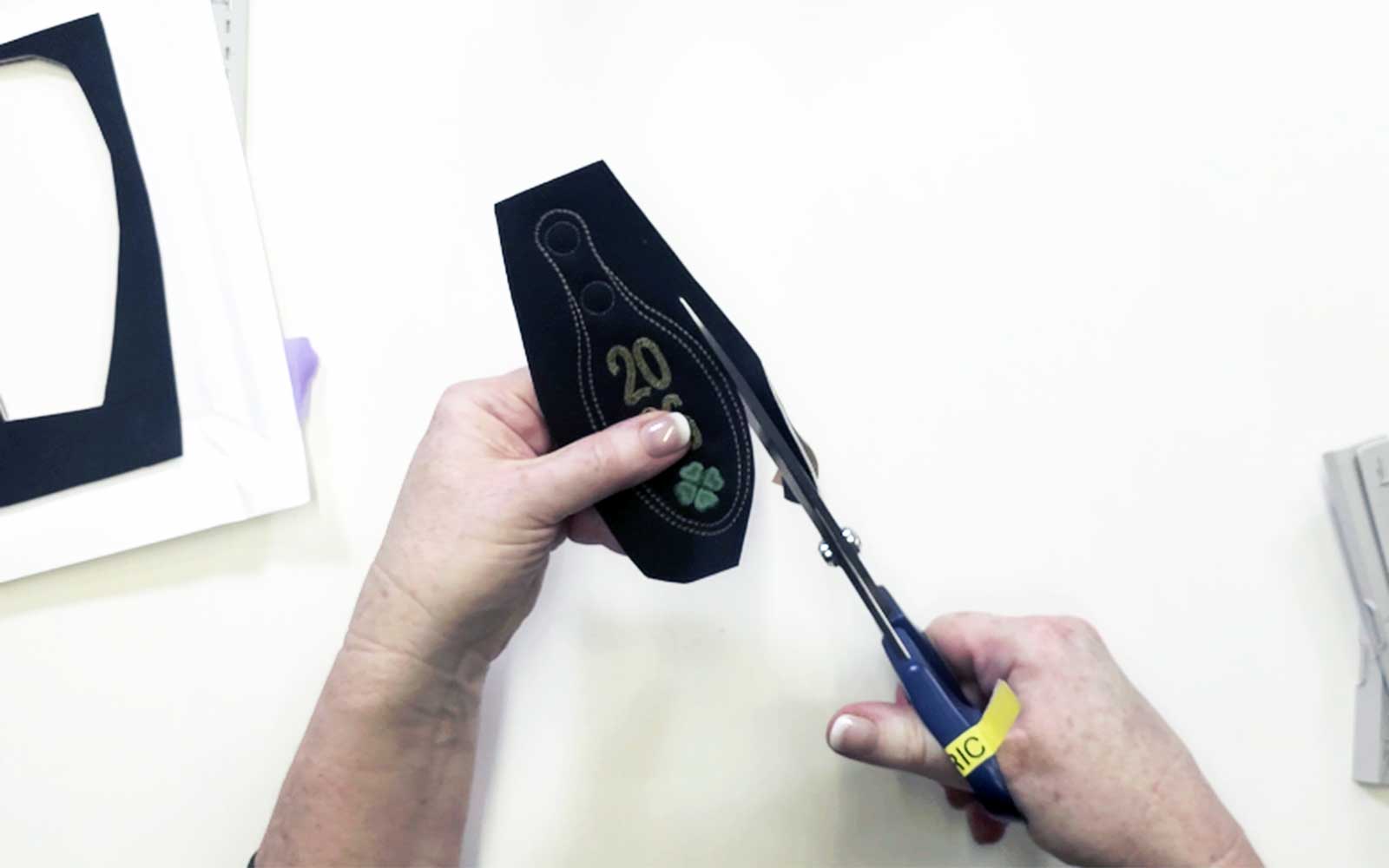 Cutting black fabric embroidered key fob with scissors