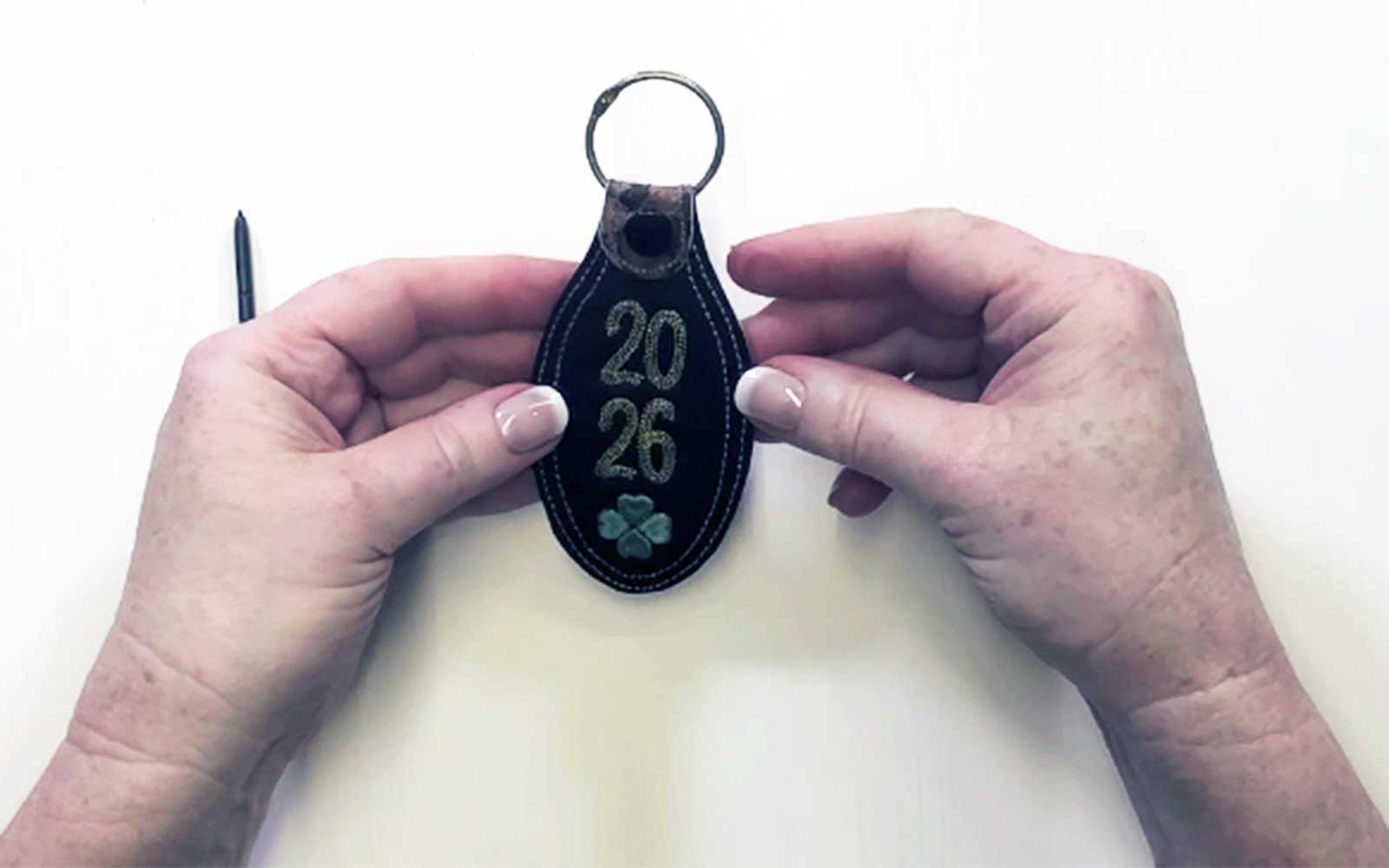 Mains tenant un porte-clés noire brodé avec 2026