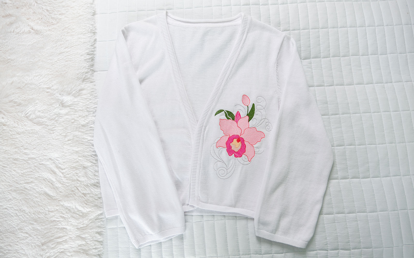 Weiße Strickjacke mit rosafarbener Orchideenstickerei auf der Brust