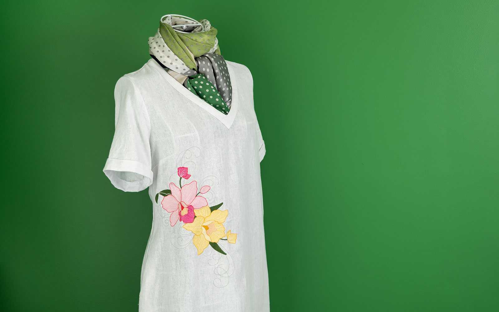 Leinenkleid mit rosa und gelber Orchideenstickerei vor dunkelgrüner Wand