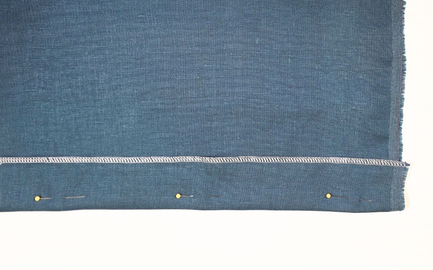 hem pinned on blue fabric with white stitching
