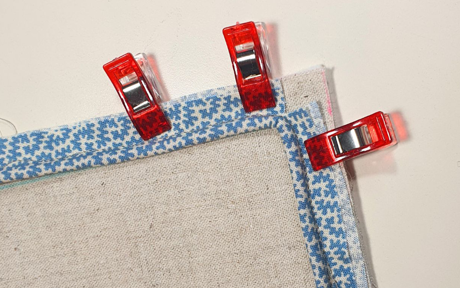 red sewing clips holding blue piping to natural linen