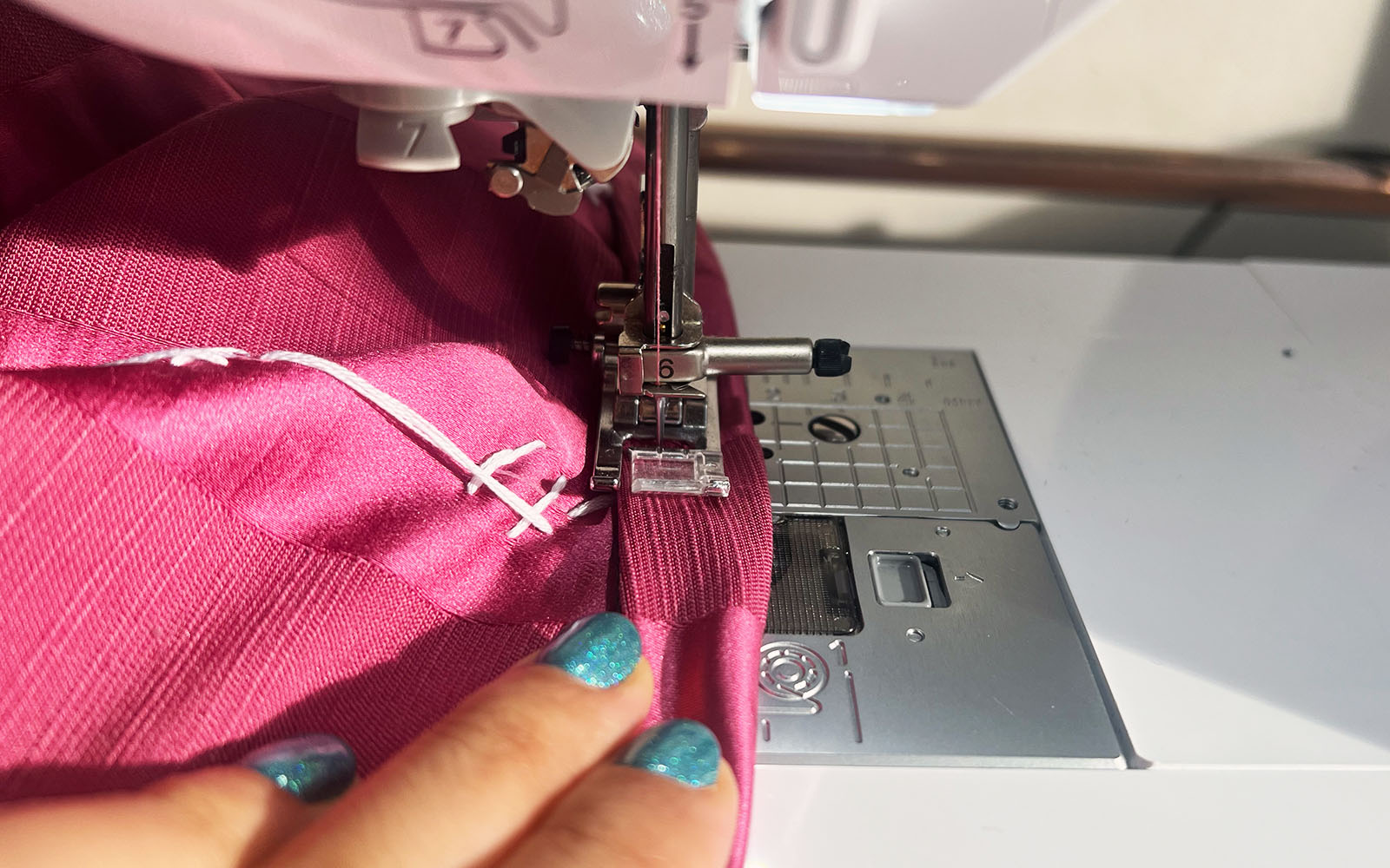 close up of hand sewing pink fabric on sewing machine