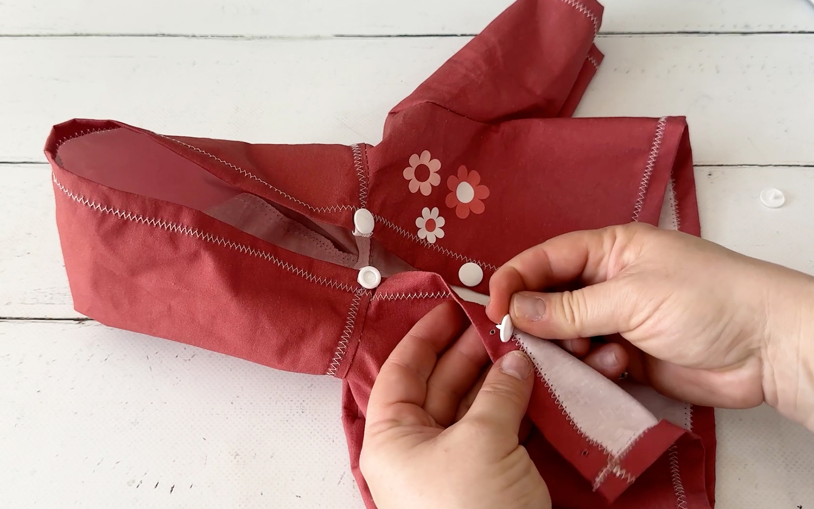 Inserting snap fasteners at front edges of doll’s hoodie