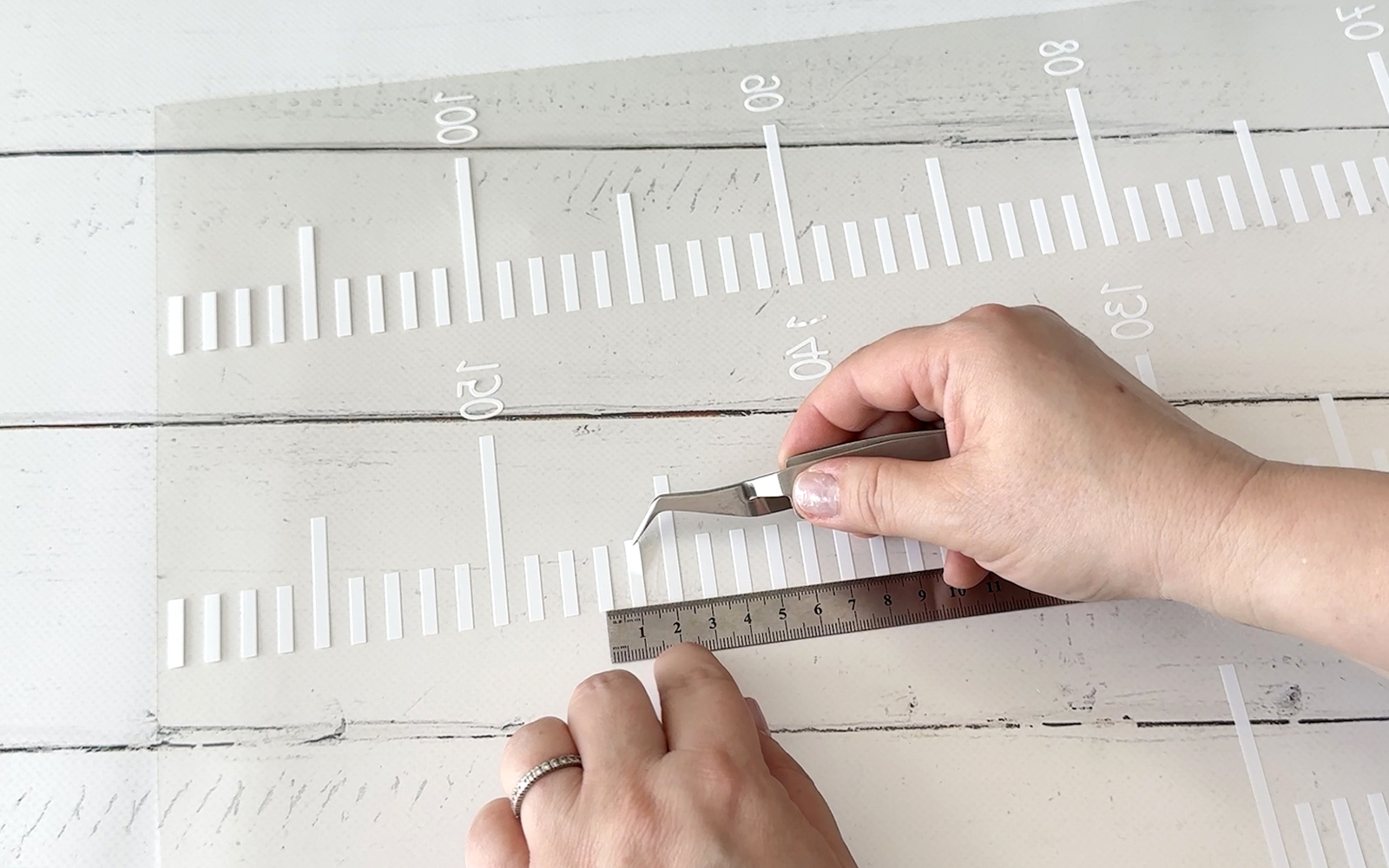 Hands holding tweezers over white flex foil chart