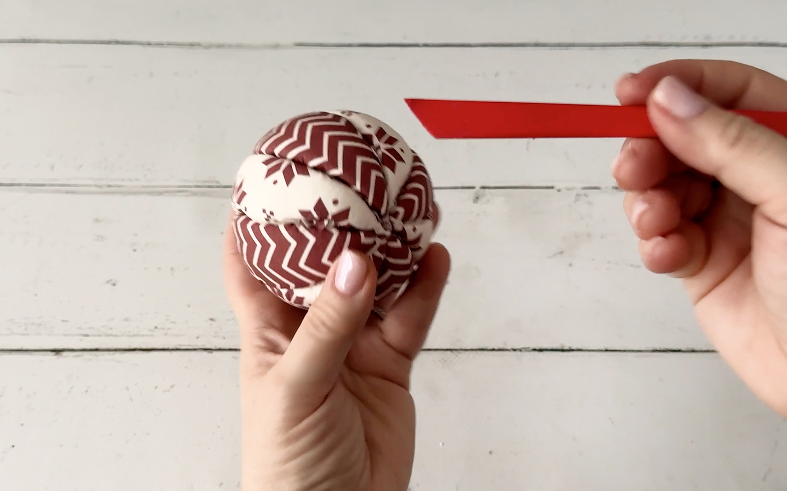 Flat tool pushing fabric edges into Styrofoam bauble
