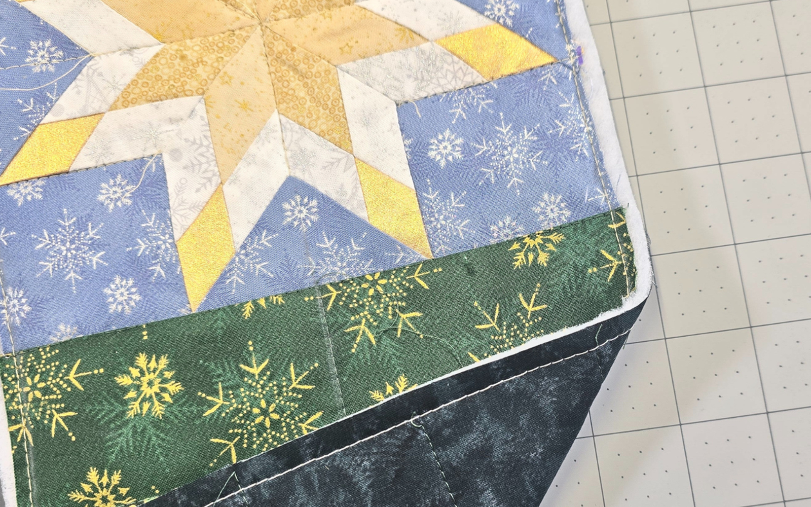 Blauw en geel sterrenquiltblok op grijze snijmat.