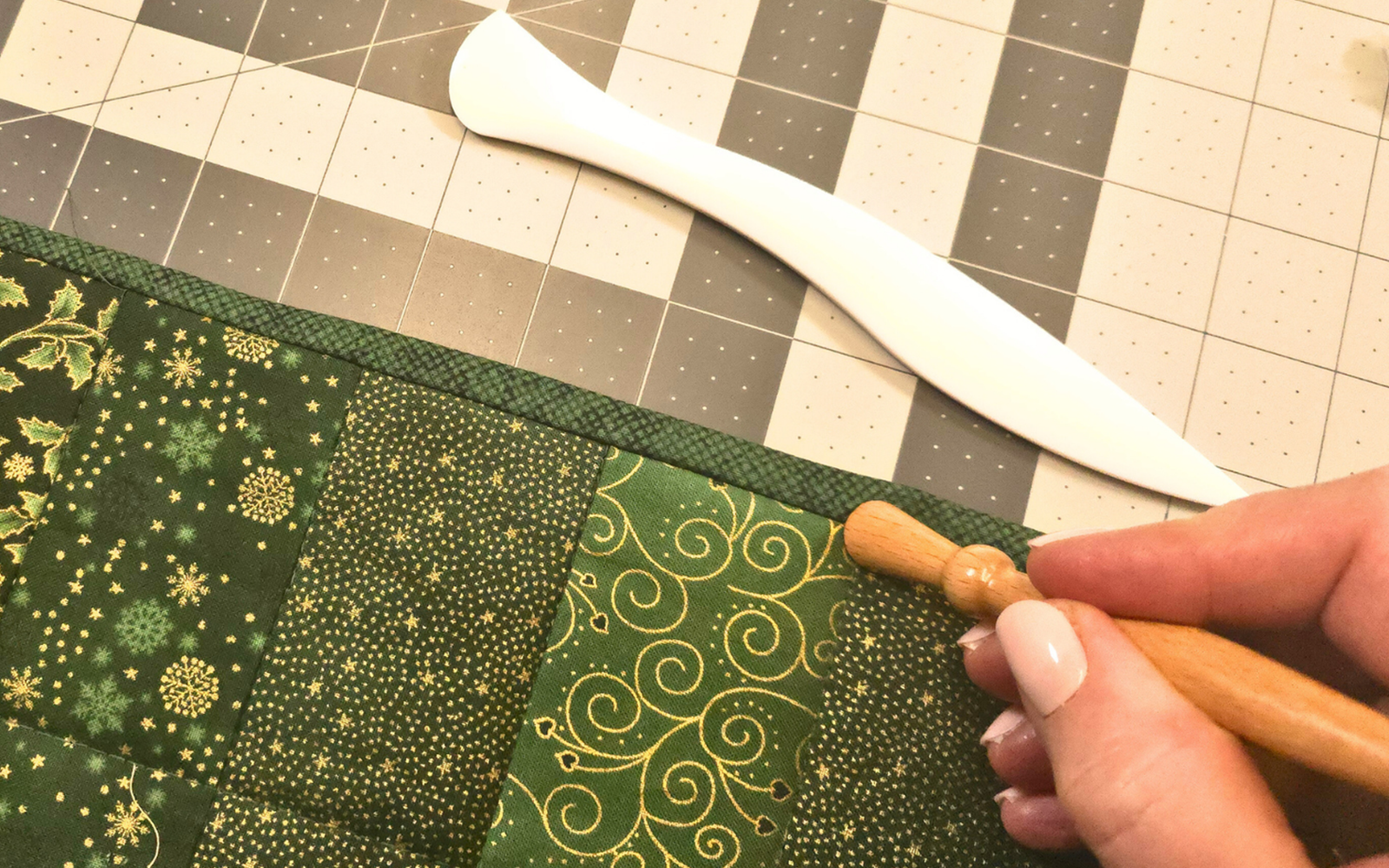 Naad met de hand strijken op groene quilt.