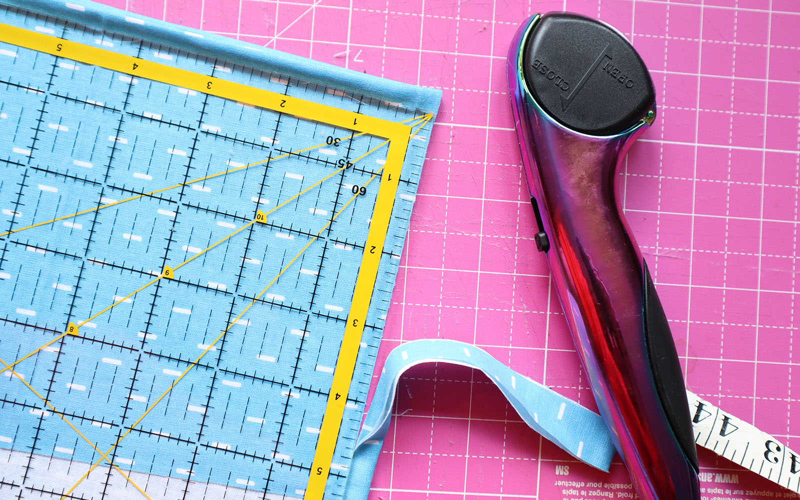 Blue fabric being cut in squares on pink cutting mat