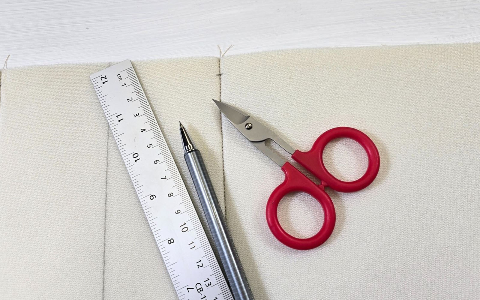 Red scissors and white ruler on fabric background