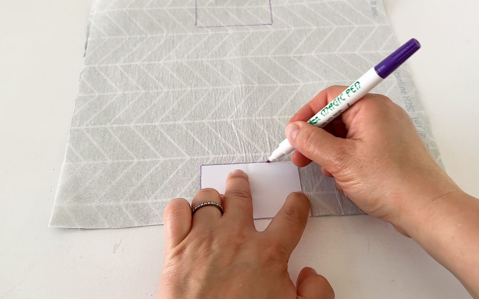 Hands drawing around paper rectangle on fabric