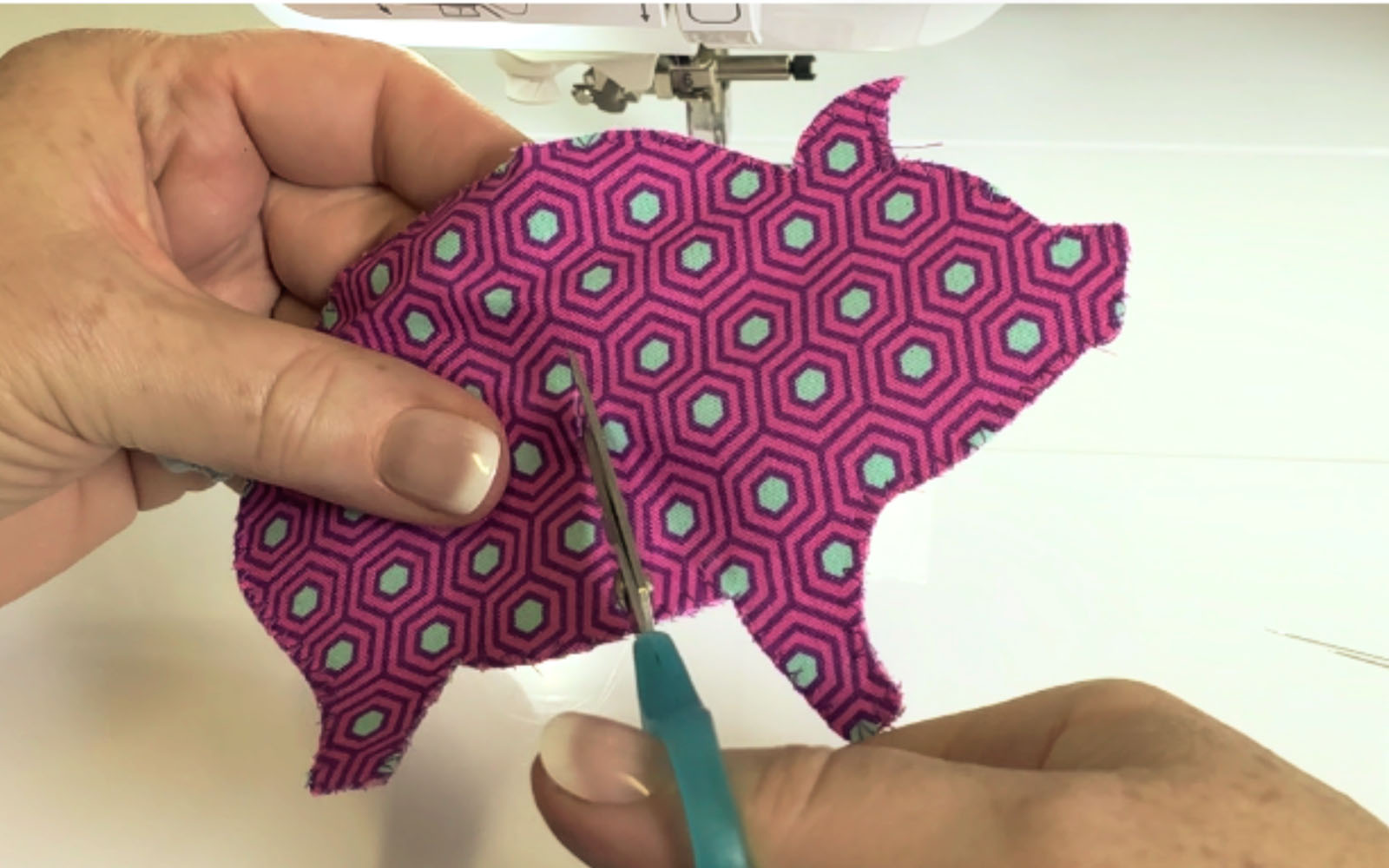 Schere in der Hand schneidet in rosa Stoffschwein