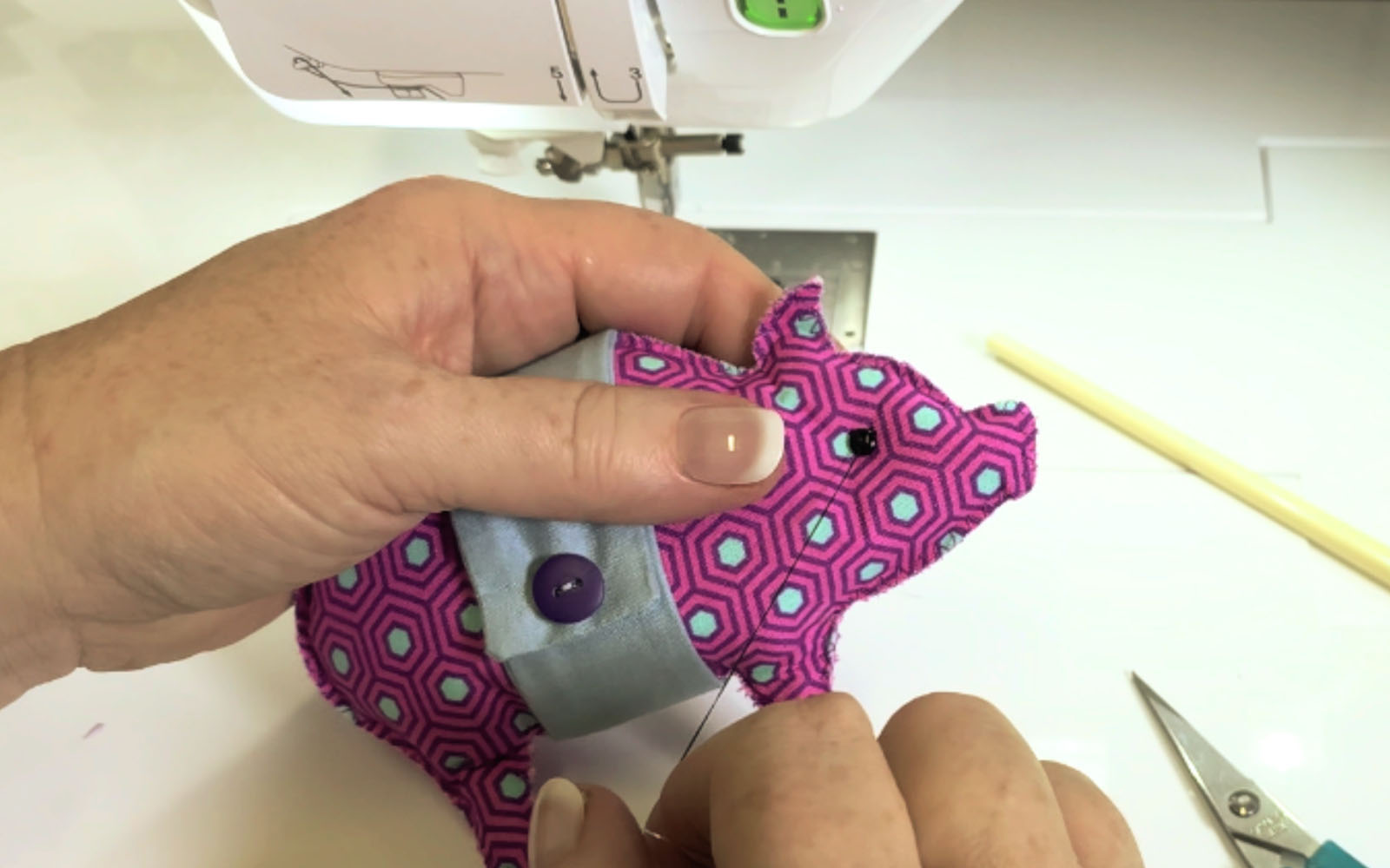 Hands sewing a black eye button on a pink fabric pig