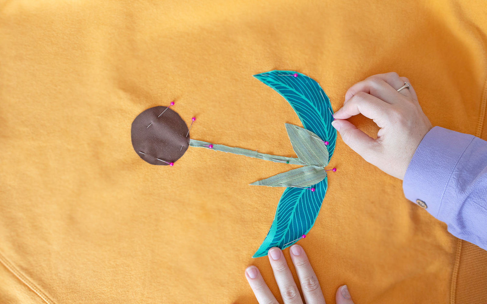 Hands placing applique shapes onto yellow jumper