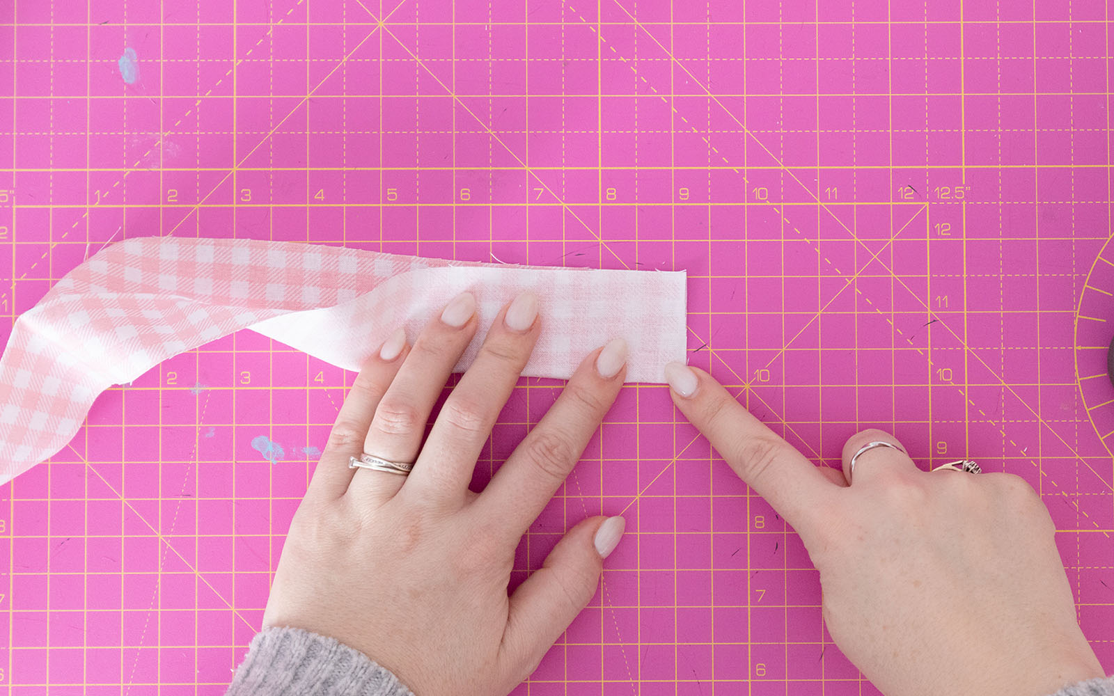 Finger pointing to edge to sew on pink gingham fabric