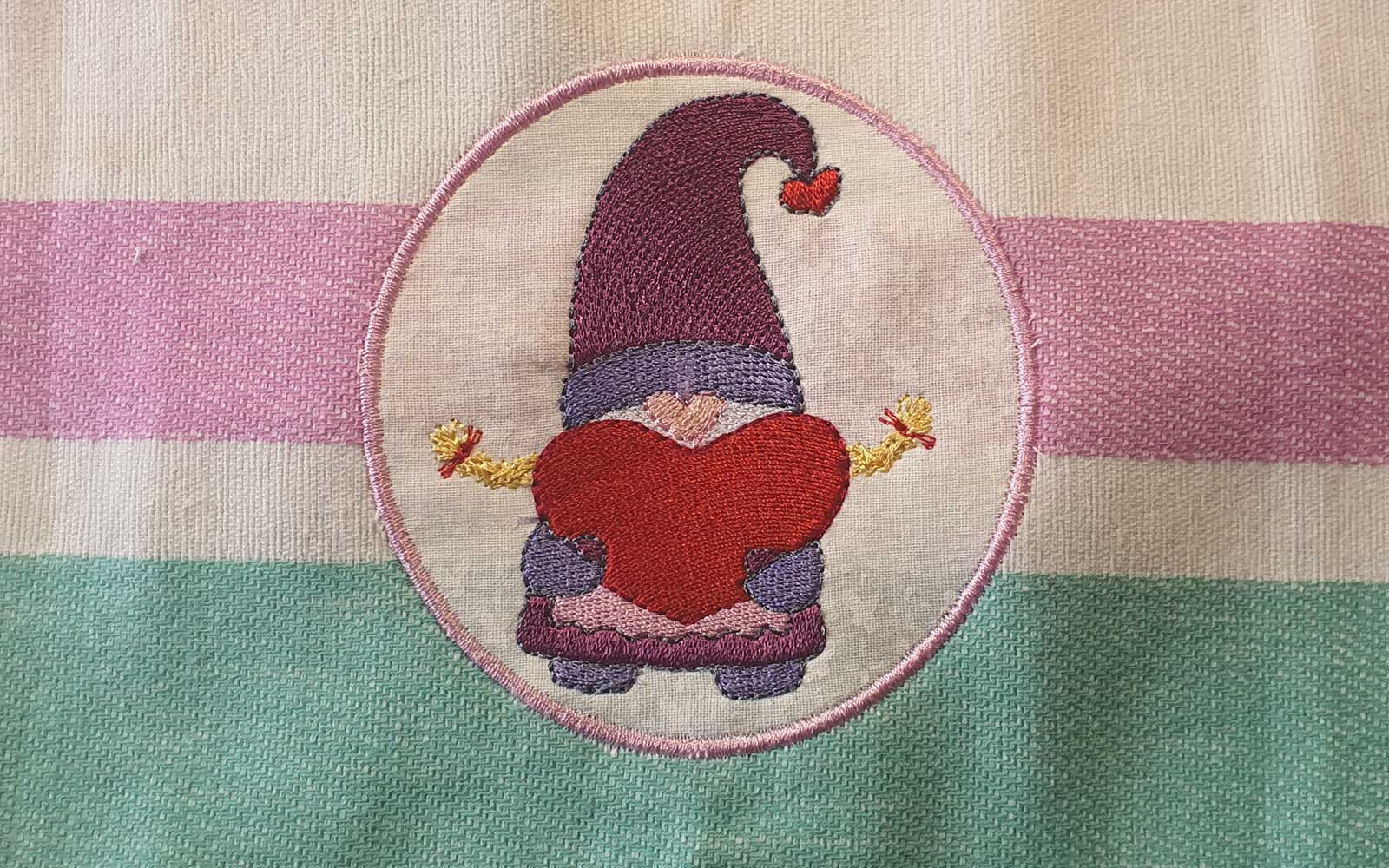 Gnome brodé tenant un cœur rouge sur un fond rayé rose et vert
