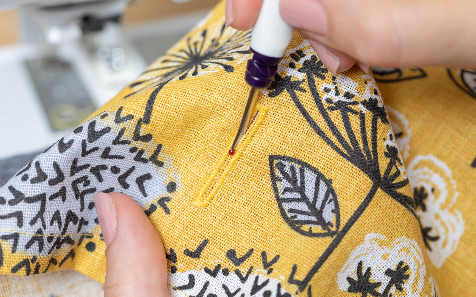 Hand holding seam ripper opening buttonhole yellow fabric