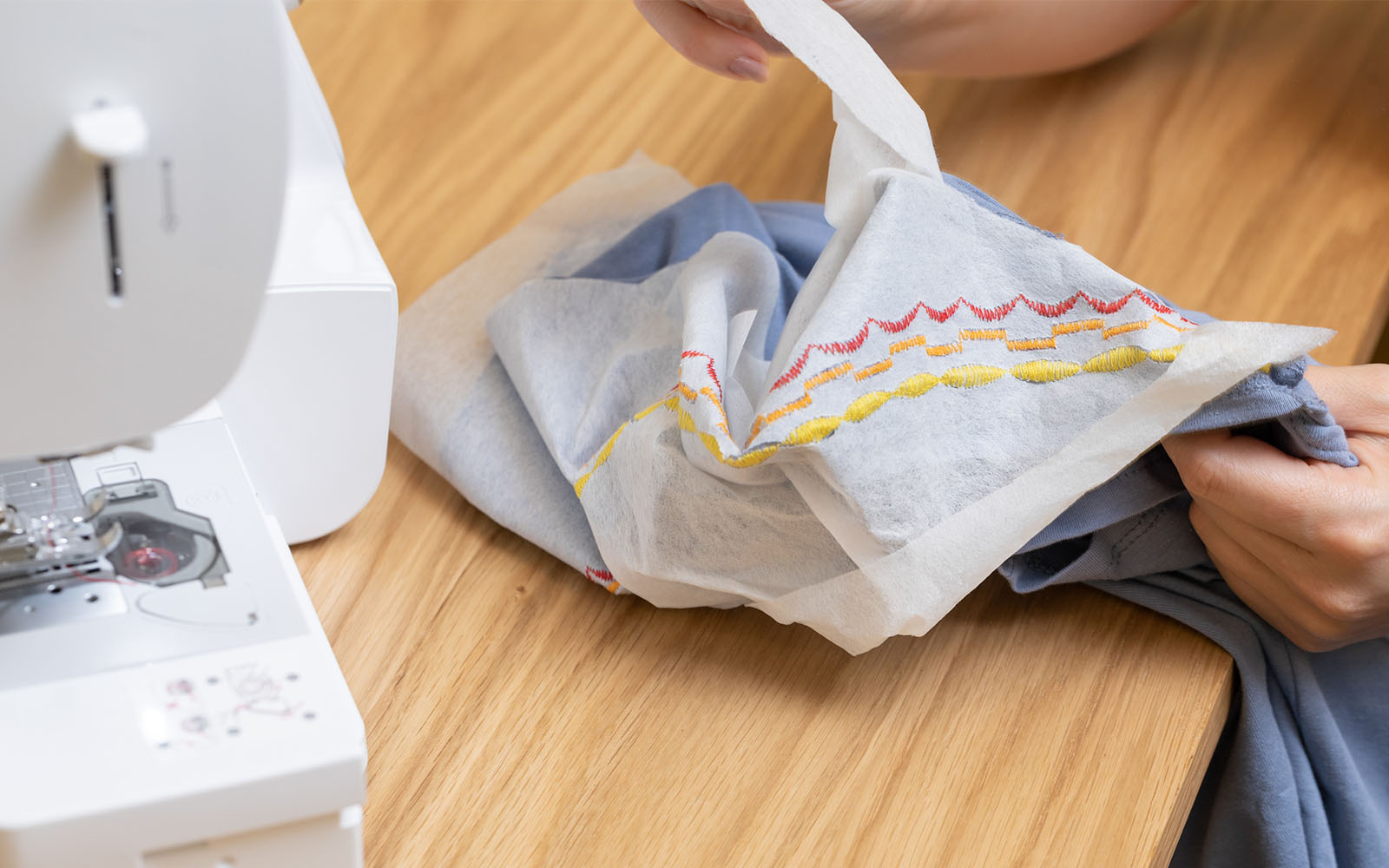 Hands tearing embroidery stabilizer from blue T-shirt