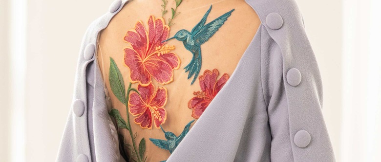 Broderie représentant un colibri bleu et une fleur rouge sur un manteau gris