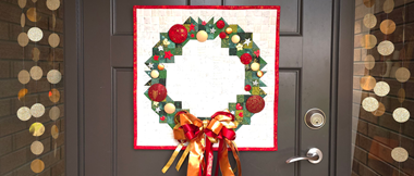 Quilt a forma di ghirlanda natalizia con fiocco rosso su porta marrone