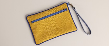 Gelbe Tasche aus Krokodil-Kunstleder mit blauem Reißverschluss und Naht auf cremefarbenem Hintergrund