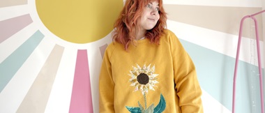 Vrouw in geel sweatshirt tegen een veelkleurige muur