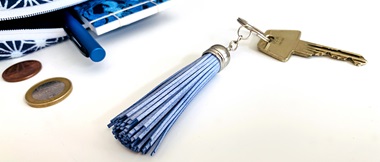 Blauw-metalen sleutelhanger met kwastje en sleutel naast open blauw tasje