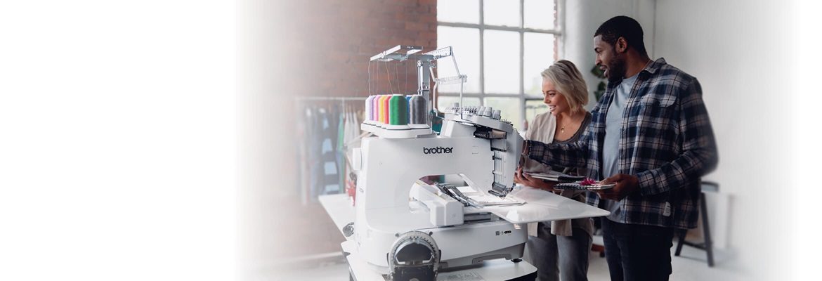 Een man en een dame gebruiken de Brother PR1055X tiennaaldsborduurmachine in een handwerkkamer